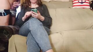 The cougar looks at the phone while giving him a hand job